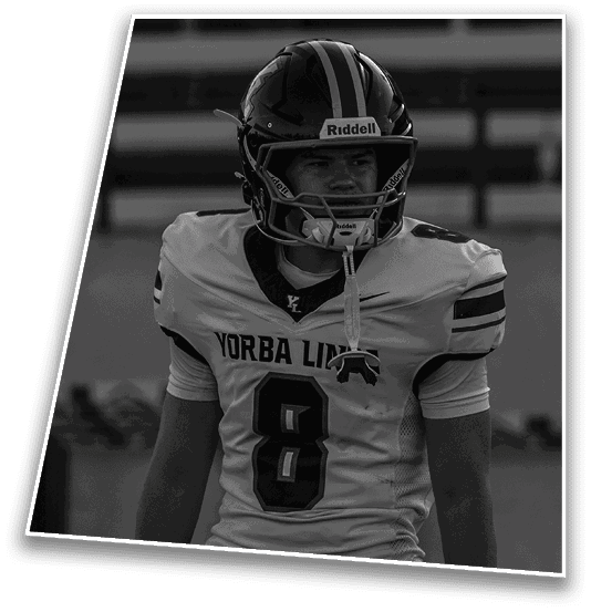A person wearing a football helmet and a jersey with the number 8 and the text “Yorba Linda" stands on a field with a focused expression. Description generated by AI