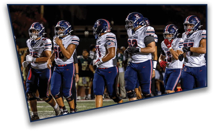 Several people wearing football helmets and uniforms stand in a row on a field at night. Description generated by AI