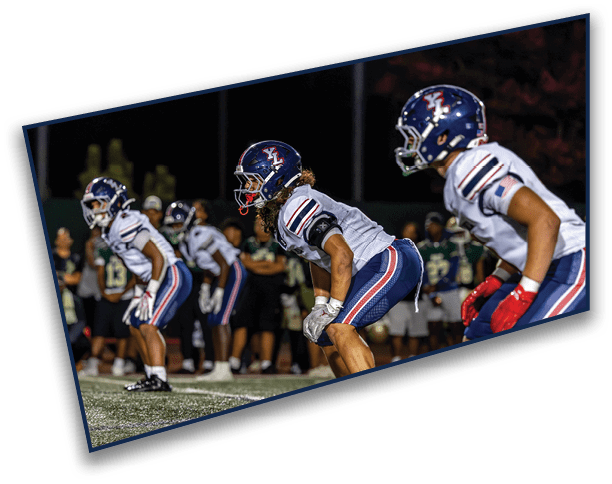 Four people in football uniforms and helmets are crouched in a ready position on a field during a nighttime game. Description generated by AI