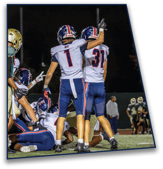 People in football uniforms are celebrating on a field at night with some players raising their arms and others on the ground. Description generated by AI