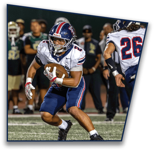 Two people in football uniforms are on a field with one holding a football while others stand in the background. Description generated by AI