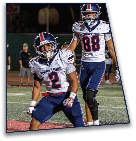 Two people in football uniforms celebrating on a field during a game at night. Description generated by AI