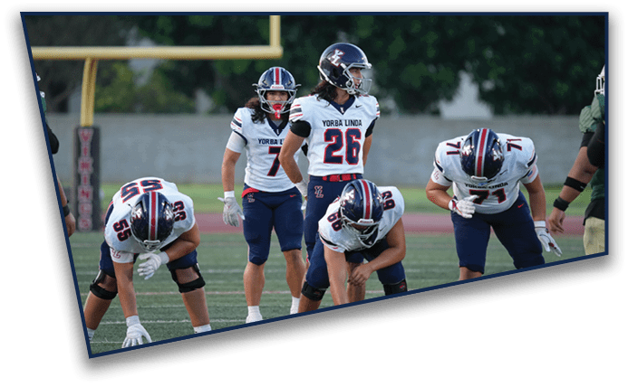 Five people in football uniforms with helmets are positioned on a field, appearing ready for a play during a game. Description generated by AI