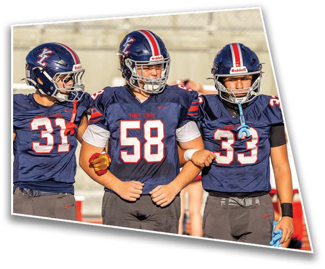 Three people in football uniforms and helmets stand side by side with their arms linked on a sports field. Description generated by AI