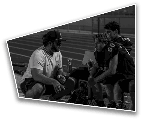 People wearing sports uniforms are gathered closely on a field at night with a blurred background of bleachers and a person walking. Description generated by AI