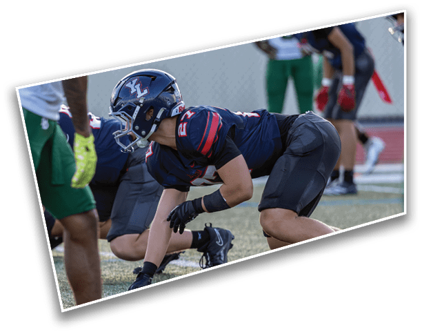People in athletic gear are crouched in a ready position on a sports field, preparing for a play. Description generated by AI