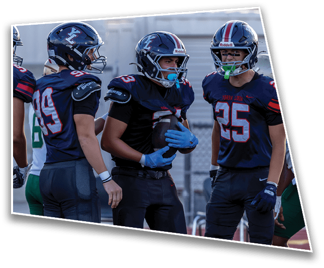 Three people wearing football helmets and uniforms are standing close together outdoors, appearing to be engaged in conversation or strategizing. Description generated by AI