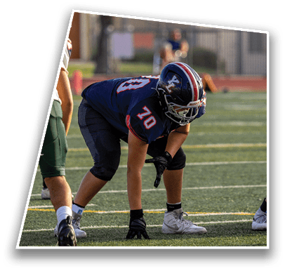 A person in a dark blue football uniform with the number 70 is crouched in a ready stance on a green football field. Description generated by AI