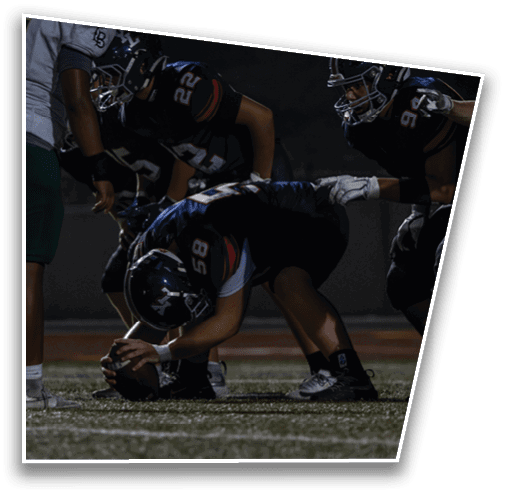 A group of people in football uniforms are positioned on a field with one person crouching and holding a football ready to snap it. Description generated by AI