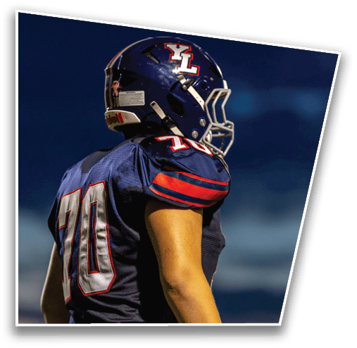 A person wearing a dark blue football uniform with the number 70 and a matching helmet is standing on a field against a dark sky. Description generated by AI