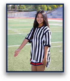 A person with long hair wearing a black and white striped shirt stands on a sports field with one arm extended to the side. Description generated by AI