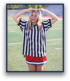 A person with long wavy hair wearing a black and white striped shirt and a red skirt stands on a sports field with arms raised above their head. Description generated by AI