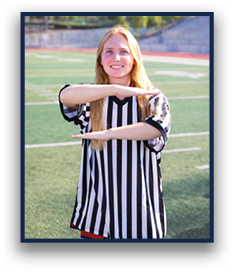 A person wearing a black and white striped referee shirt is standing on a sports field making a timeout gesture with their arms. Description generated by AI