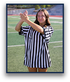 A person wearing a black and white striped referee shirt is standing on a sports field with hands raised and clasped together. Description generated by AI