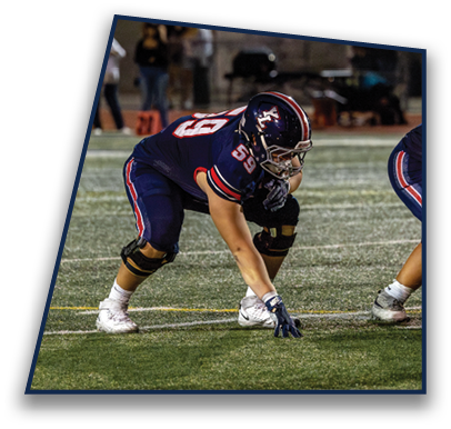 A person in a dark blue football uniform with the number 53 is crouched in a ready stance on a football field during a game. Description generated by AI