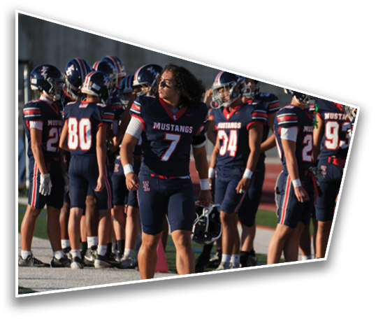 A group of people wearing navy blue football uniforms with “Mustangs" written on them are gathered on a field, with one person in the foreground looking to the side. Description generated by AI