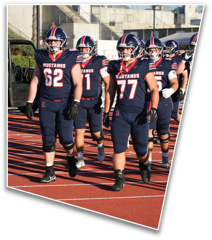 Three people wearing navy blue football uniforms with red and white accents and helmets stand together on a field with a concrete structure in the background. Description generated by AI