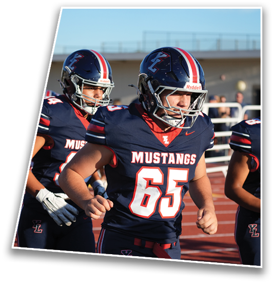 Two people wearing navy blue Mustangs football uniforms and helmets are running on a track near bleachers. Description generated by AI