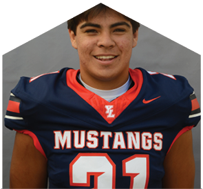 A person wearing a navy blue football jersey with red and white accents and the word Mustangs across the chest is smiling against a plain gray background. Description generated by AI