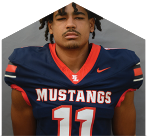 A person with curly hair wearing a navy blue and red football jersey with the word Mustangs and the number 11 stands against a gray background. Description generated by AI