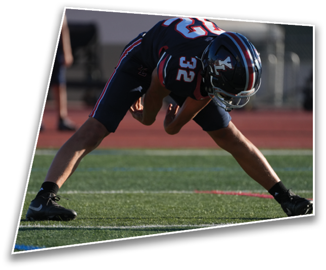 A person wearing black athletic shoes is standing with legs wide apart on a green sports field with multiple colored lines. Description generated by AI