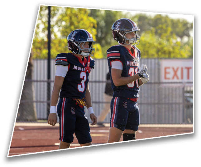Two people wearing dark football helmets with a white “L" logo are outdoors with trees in the background. Description generated by AI