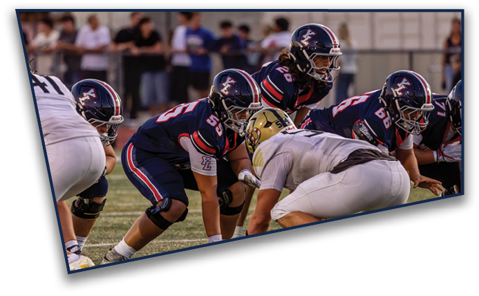 Several football players in helmets and uniforms are lined up on a field preparing for a play during a game. Description generated by AI