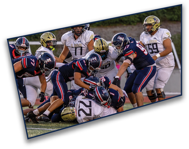 A group of football players in dark and white uniforms are engaged in a tackle on the field during a game. Description generated by AI