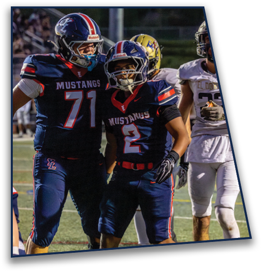 Two people in dark blue football uniforms with “Mustangs" on the jerseys are standing on a field near a football, with one person in white sportswear nearby. Description generated by AI