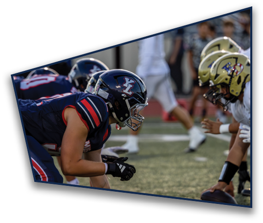 Several people wearing football helmets and uniforms are on a field with a blurred background including a referee and other individuals. Description generated by AI