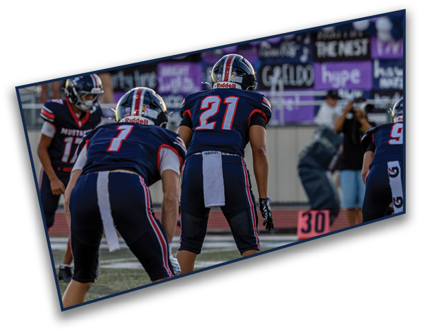 Four people in football uniforms are positioned on a field, appearing to prepare for a play during a game. Description generated by AI