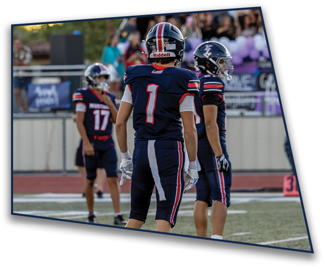 People in football uniforms are on a field with a crowd of spectators in the background during a game at sunset. Description generated by AI