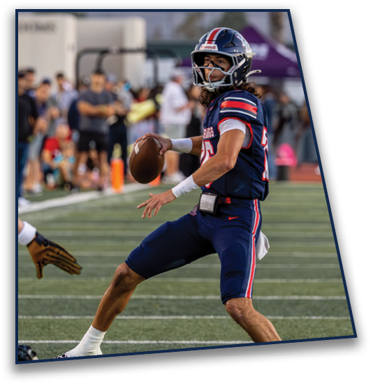 A person wearing a blue football uniform and helmet is preparing to throw a football on a field with spectators in the background. Description generated by AI
