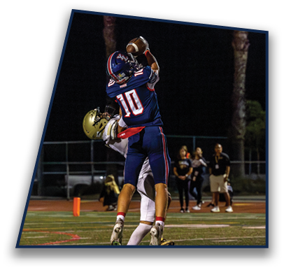 Two people in football uniforms are jumping to catch a ball on a field at night with spectators in the background. Description generated by AI