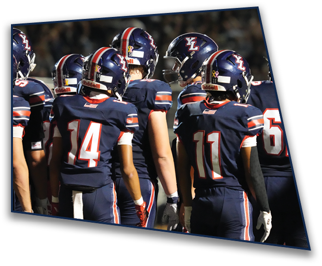 A group of people wearing navy blue football uniforms with helmets are gathered closely together on a field. Description generated by AI