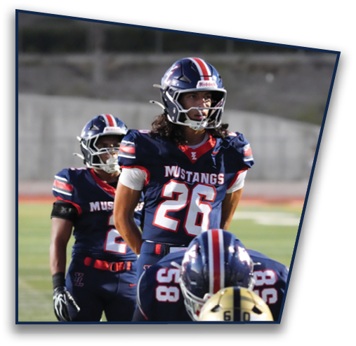 Adults wearing navy blue football uniforms with red and white stripes and helmets are standing on a football field during a game or practice. Description generated by AI
