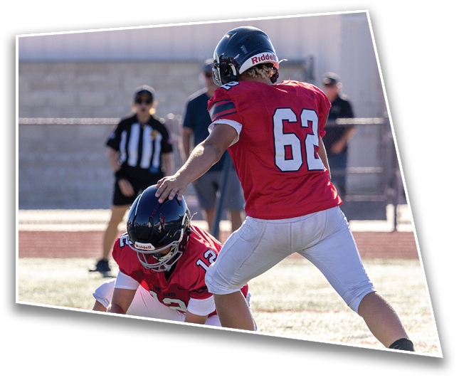 A person wearing a red football jersey with the number 62 and a black helmet is on a field with blurred people and trees in the background. Description generated by AI