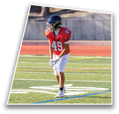 A person wearing a red sports jersey with the number 49 and white pants is standing on a green football field near a blue line. Description generated by AI