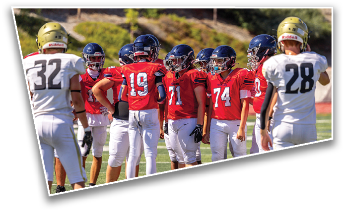 A group of people wearing red and white football uniforms and helmets are gathered on a grassy field, seemingly preparing for a play. Description generated by AI