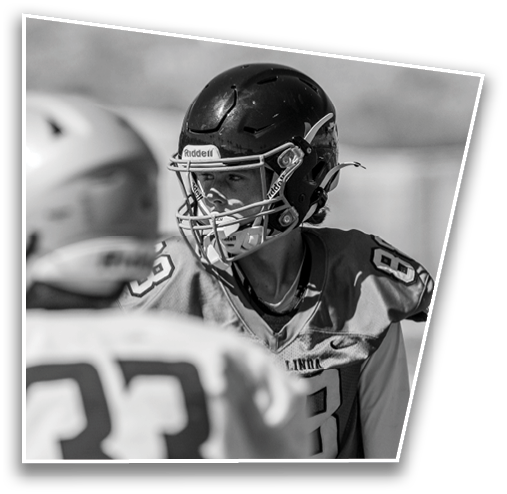 Two people wearing football helmets and jerseys are engaged in a conversation or interaction on a sports field. Description generated by AI