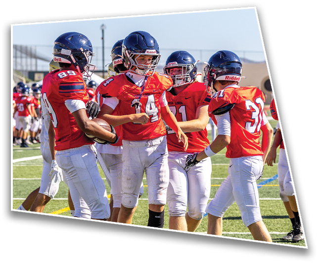 A group of people wearing red football uniforms and helmets are gathered on a field, appearing to celebrate or strategize during a game. Description generated by AI