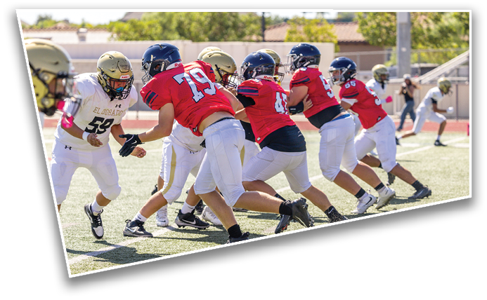 Several people wearing football uniforms are gathered on a field, with one person in a white and green uniform facing others in dark blue and red uniforms. Description generated by AI