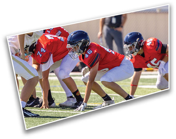 People in red and white football uniforms are crouched in a ready position on a grassy field during a game. Description generated by AI