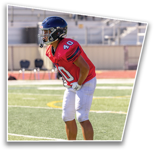 A person wearing a red sports jersey with the number 40 and a dark helmet is on a field with blurred spectators in the background. Description generated by AI