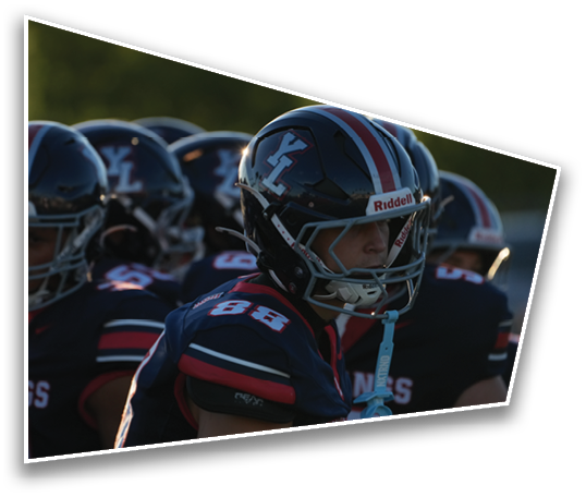 People wearing football helmets and uniforms are gathered closely together, appearing focused and ready for a game. Description generated by AI