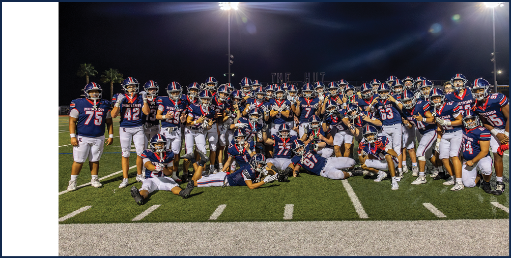 A large group of people wearing matching football uniforms pose together on a well-lit field at night. Description generated by AI