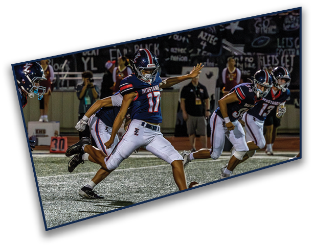 Several people in football uniforms are actively playing on a field, with one person in the center kicking a football. Description generated by AI