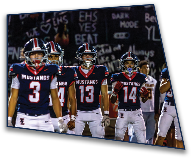Four people wearing navy blue football jerseys with “MUSTANGS" written on them stand on a field, appearing focused and ready for action. Description generated by AI