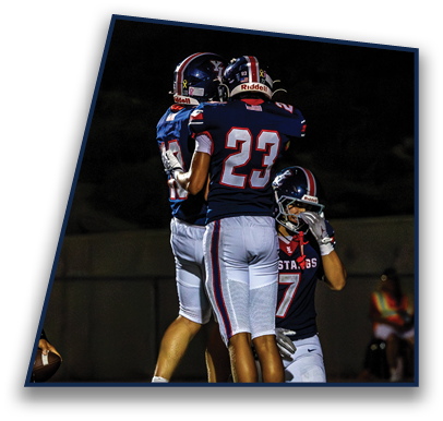Two people in football uniforms are celebrating on a field while a third person in a football uniform kneels nearby. Description generated by AI