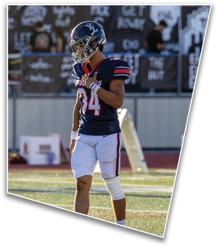 A person wearing a football uniform with the number 34 stands on a field holding their helmet strap. Description generated by AI